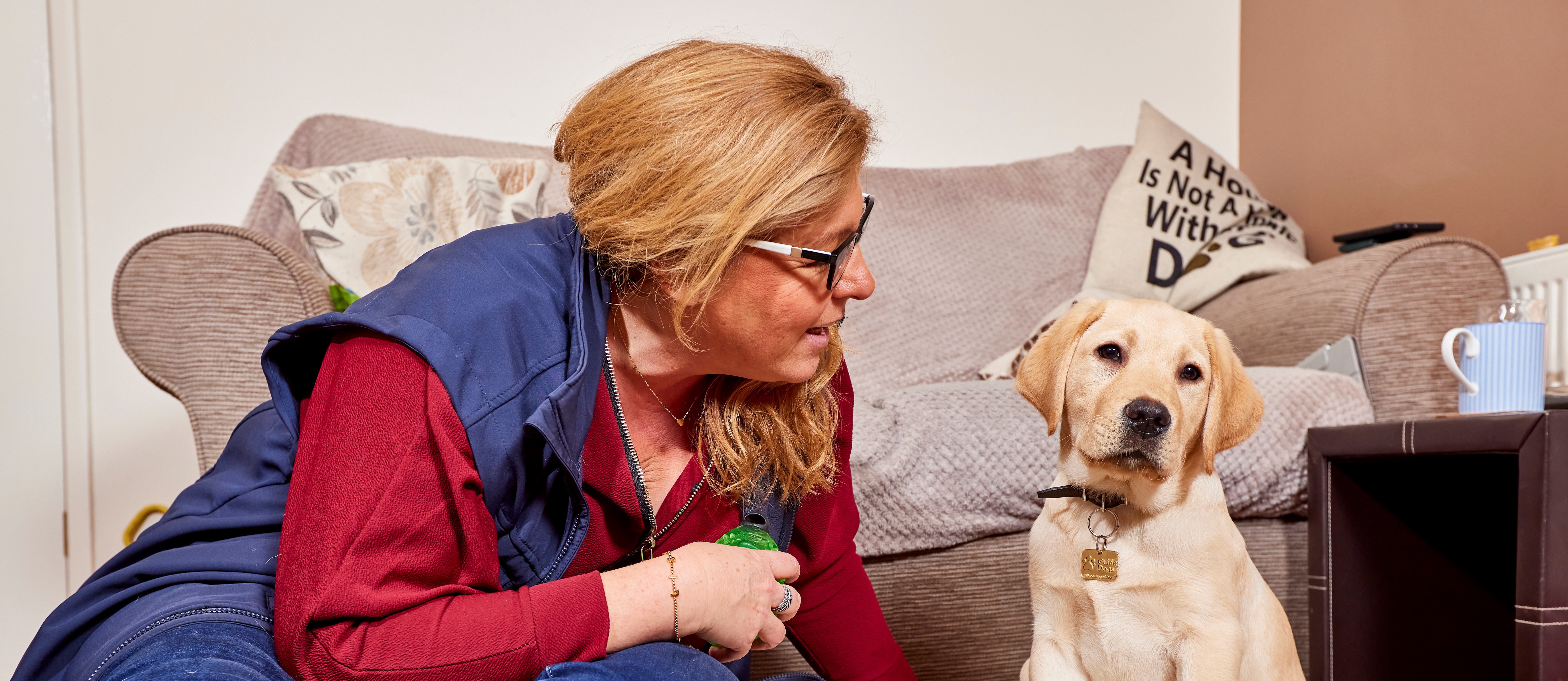 An image of a Puppy Raiser Lisa, sat on the floor next to puppy Archie. 