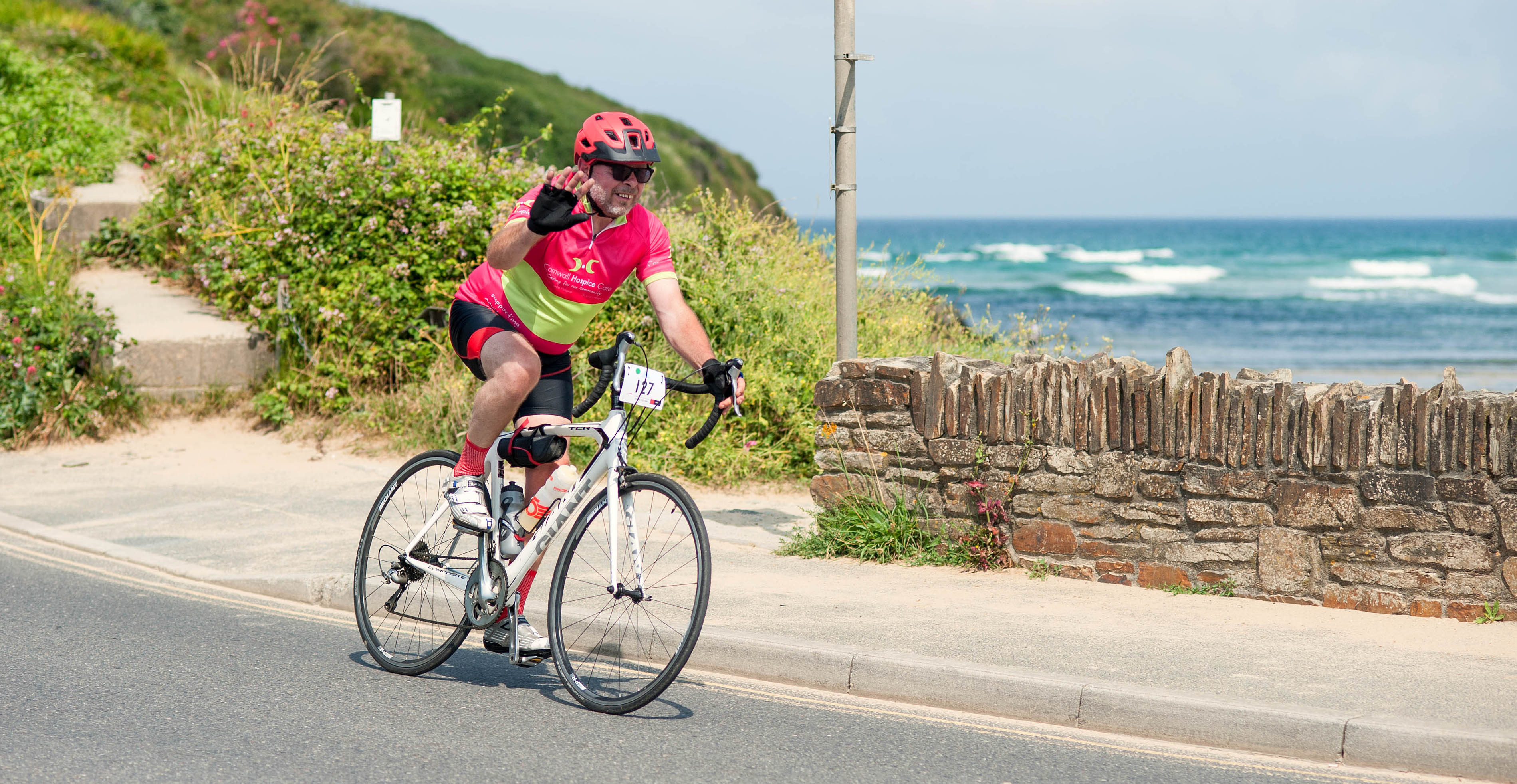 Coast and Clay Cycle Sportive - fundraiser cycling and waving as they pass scenic beach backdrop