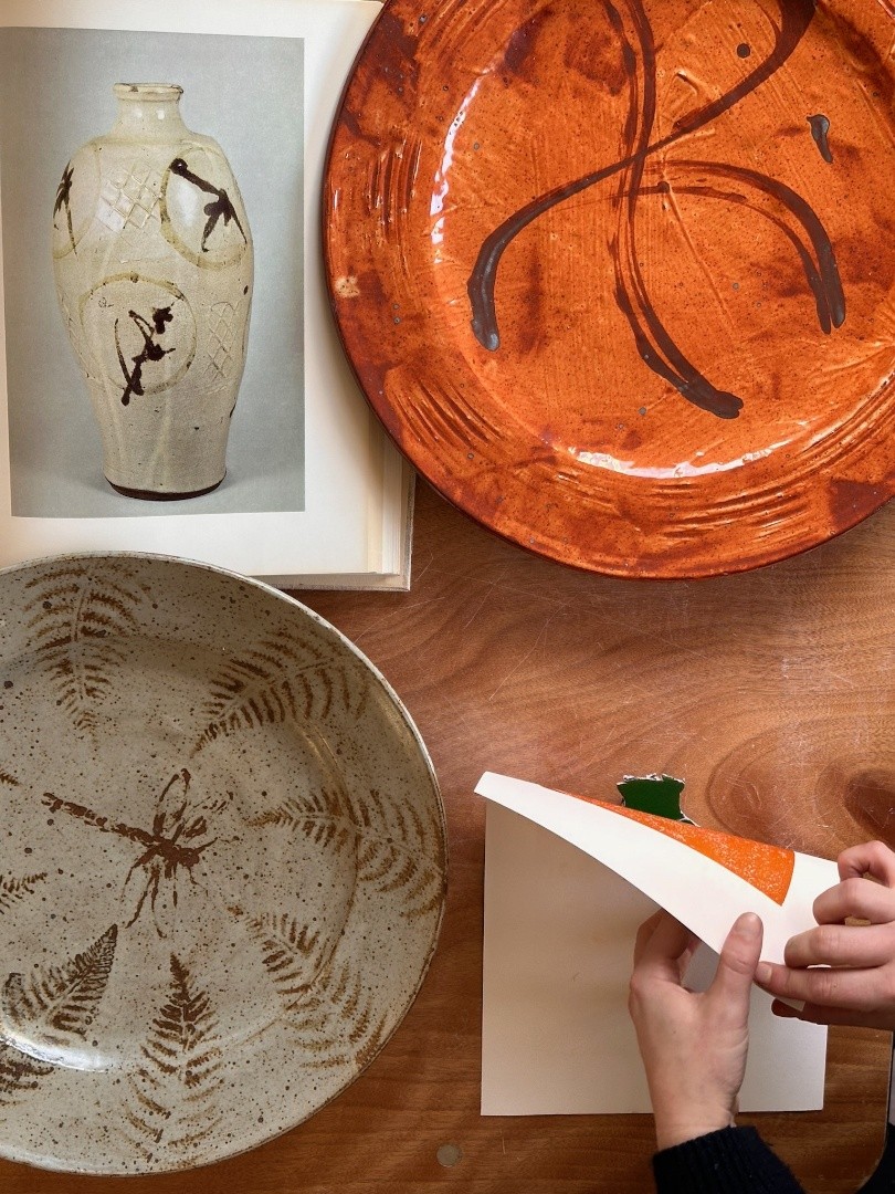 A photograph of one of our creative workshops at Leach Pottery with 2 patterned plates (one terracotta, one grey) and a photo of a Bernard Leach vase as inspiration.