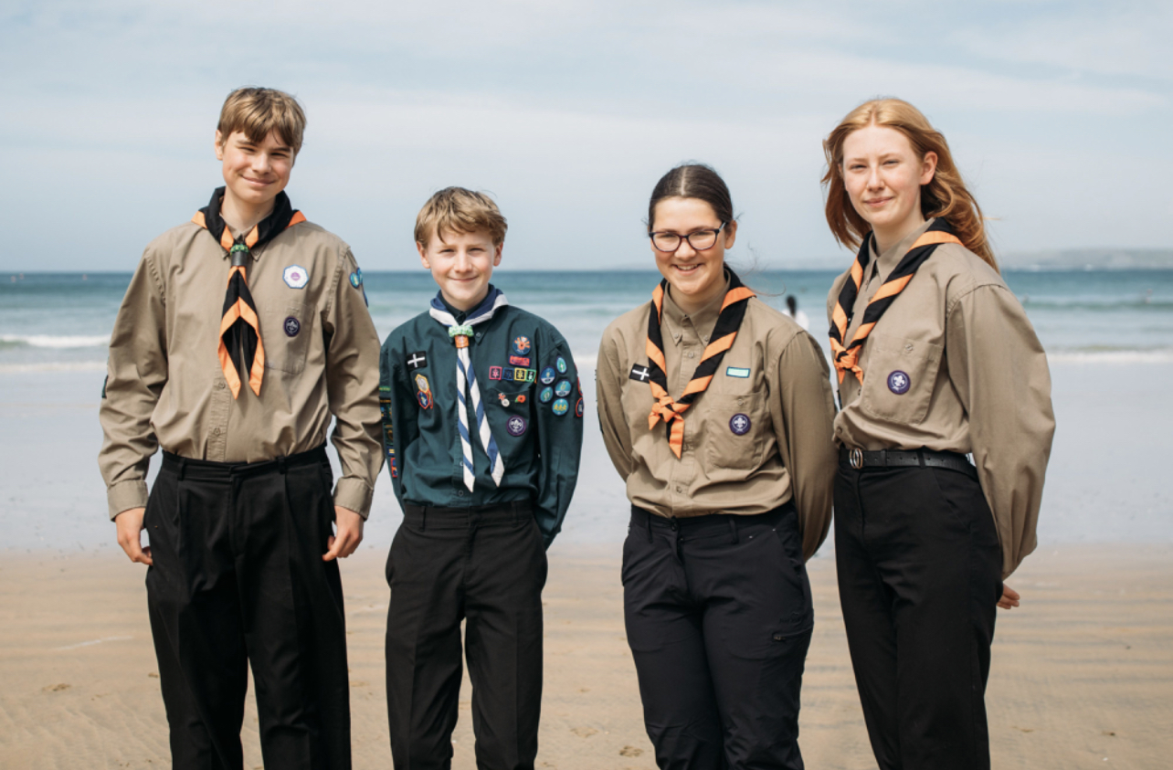 Four young people stood on a beach in Scouts uniform