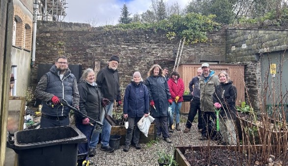 Group of people in a community garden, holding tools, looking proud.