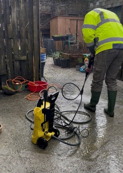Person in High visibility vest jet washing the ground
