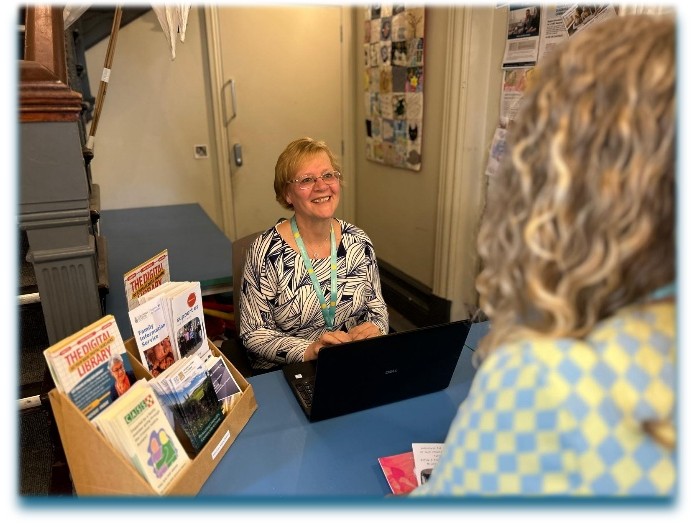 Welcoming volunteer sat at desk, smiling at visitor