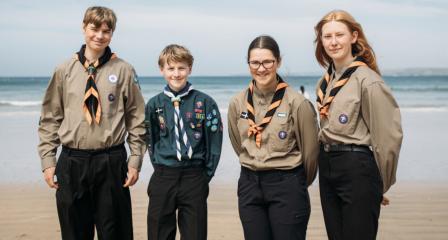 Four young people stood on a beach in Scouts uniform