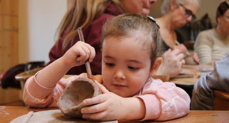 A child in a pink jumper decorates egg cups as part of a family workshop