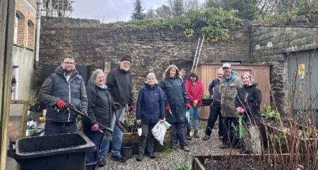 Group of people in a community garden, holding tools, looking proud.