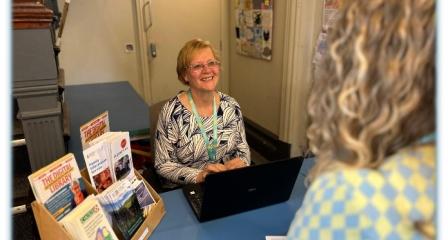 Welcoming volunteer sat at desk, smiling at visitor